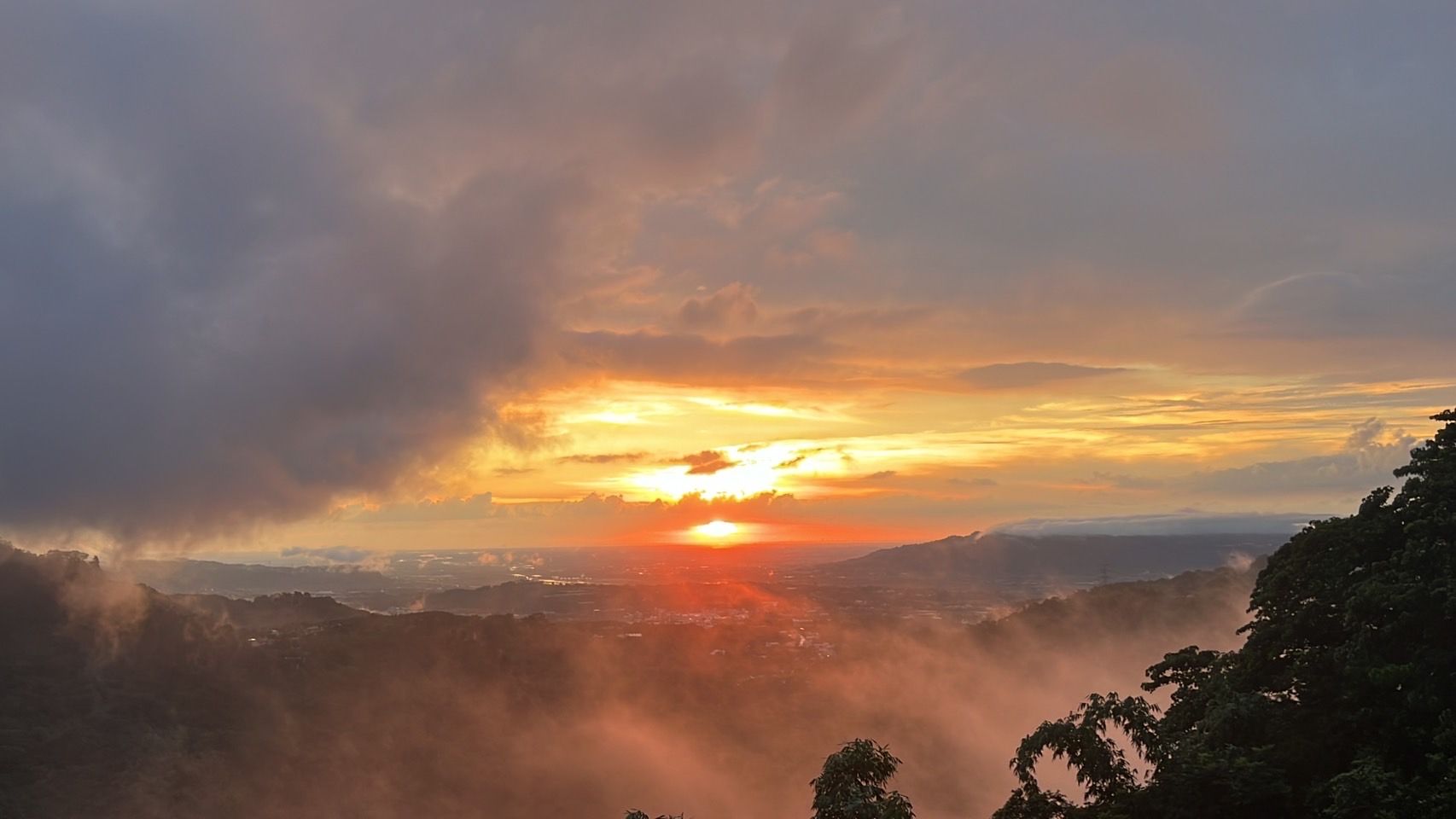夕陽自山谷落下，晚霞染紅雲層，霧氣漫過樹梢